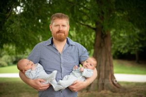 Newborn twins held by Dad outdoors
