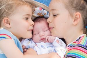 Newborn and siblings kissing portrait