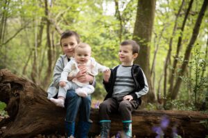 Outdoor family photoshoots in the bluebells - 2 brothers and baby sister on a log