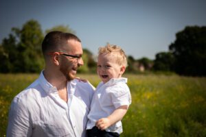 Outdoor family photos in the sun with Toddler and dad laughing in field