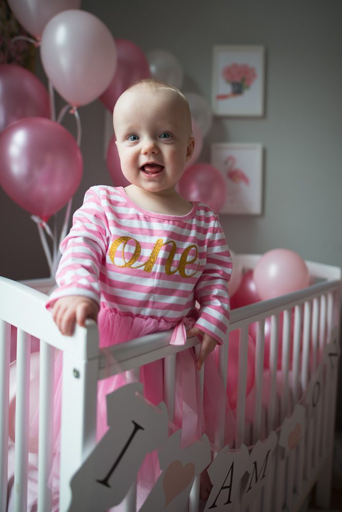baby photography at home, one year old girl in cot with birthday decorations