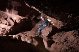 boy climbing through muddy rock in cave